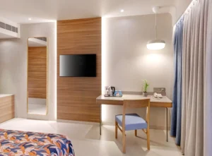 Hotel Tunga Regale luxury guest room in Andheri East, Mumbai, with modern wood paneling, wall-mounted TV, work desk, designer chair, pendant lamp, and elegant decor.