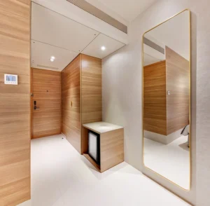 Hotel Tunga Regale modern suite in Andheri East, Mumbai with light wood paneling, floor-to-ceiling mirror, minimal furniture, ambient lighting, and a compact minibar.