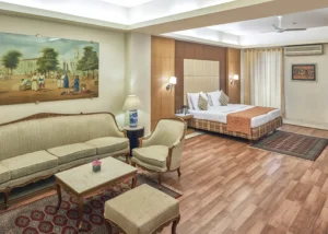 Hotel Astoria luxury suite in Mumbai with king-size bed, elegant vintage sofa set, wood-panel headboard, modern lighting, cozy rugs, and warm neutral decor.