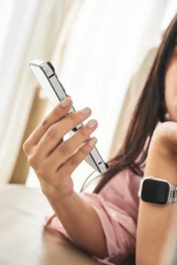 Woman holding a smartphone with a square-faced smart watch on her wrist, focusing on her hand, watch, and the side of her face.