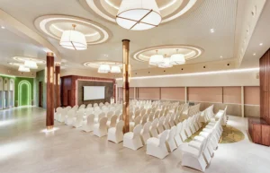 Hotel Tunga Regale modern banquet hall with elegant lighting, rows of white chairs, projector screen, wood-paneled accents, and spacious interiors in Andheri, Mumbai.