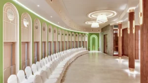 Hotel Tunga Regale modern banquet hall with elegant lighting, rows of white chairs, projector screen, wood-paneled columns, and spacious interiors in Andheri, Mumbai.