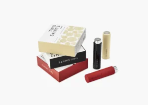 Two Saints luxury fragrance set with three sleek refillable atomizers (black, gold, red) and elegant nested boxes in red, black, and gold.
