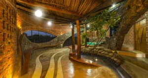 Wada Brick House interior with curved exposed brick walls, stone staircases, wooden ceilings, natural indoor landscaping, and warm ambient lighting.