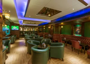 Hotel GCC elegant bar lounge with green leather chairs, wooden decor, ambient lighting, and a stocked bar counter in Mumbai.