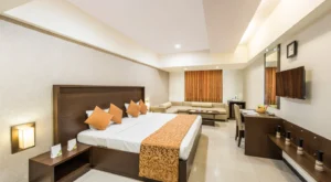 Hotel GCC spacious luxury room with king-size bed, plush orange décor, modern furniture, work desk, flat-screen TV, and comfortable seating area in Mumbai.