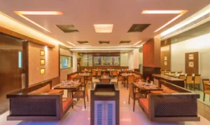 Hotel Tunga Regenza luxury restaurant with elegant wooden seating, modern lighting, set tables, and a large aquarium centerpiece in Navi Mumbai.
