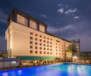 Hotel GCC exterior view at dusk with illuminated swimming pool, modern architecture, and palm trees in Mumbai, India.