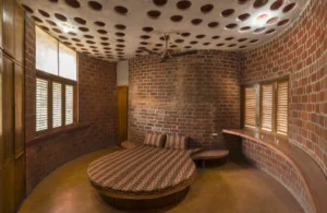Wada Brick House bedroom with curved exposed brick walls, a round patterned bed, perforated white ceiling with circular vents, and wooden accents.