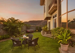 Sajala luxury villa garden at sunset with manicured lawn, modern patio furniture, lush green plants, and a scenic mountain view in Mumbai.
