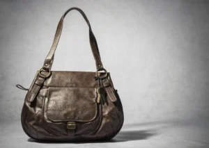 Brown leather Baggit handbag with dual shoulder straps, gold-tone hardware, front flap pocket, and hanging keychain, displayed on a plain background.