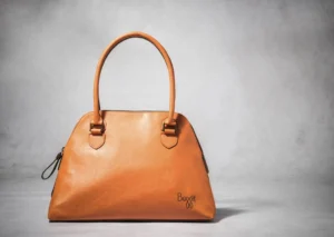 Baggit tan leather handbag with twin handles, minimalist design, and subtle logo displayed on a light grey background.