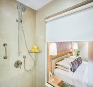 Contemporary glass-walled bathroom with shower and window overlooking a luxurious hotel bedroom at Hotel Bawa International.