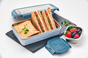 Pratap Plastic lunchbox with whole wheat sandwiches and fresh berries on a clean background.